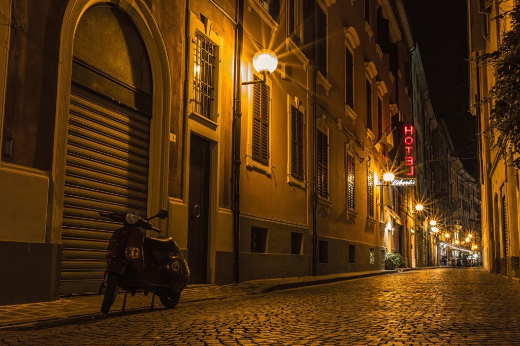 A Scooter on a cobble stone street at night.